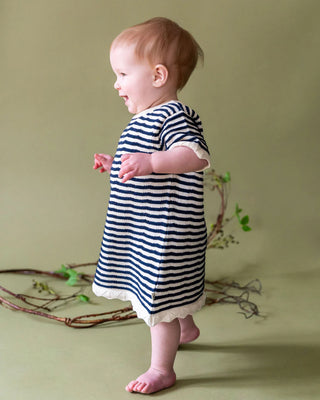 Baby wearing a striped dress standing on a green background