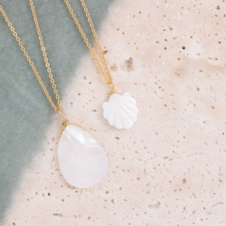 Necklace with white pendant and gold chain on textured surface