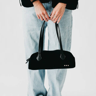 Person holding a black handbag with a plain background