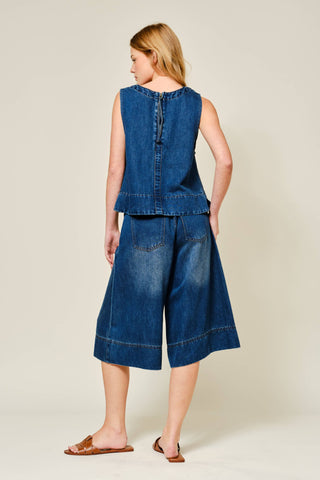 Woman wearing a blue denim sleeveless top and wide-leg pants on a beige background