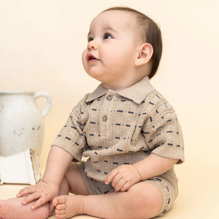 Baby wearing a beige patterned outfit sitting on a light-colored surface.