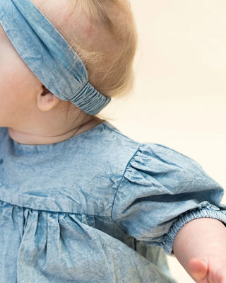 Baby wearing a blue dress and headband on a light background