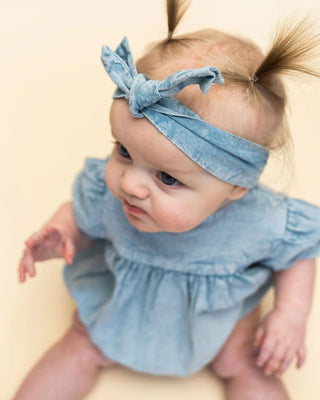 Baby wearing a denim outfit and headband on a beige background