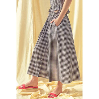 Person wearing a black and white checkered skirt with red sandals on a yellow fabric background