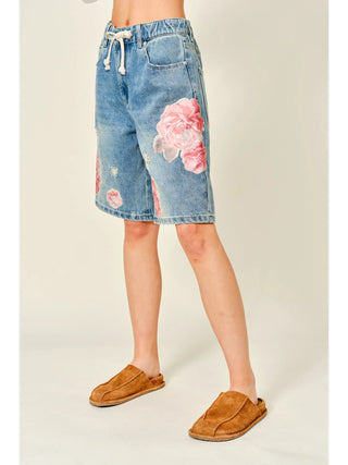 Denim shorts with floral designs worn by a person on a plain background