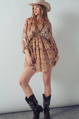 Woman wearing a floral dress, cowboy boots, and a hat against a plain background