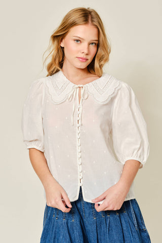 Woman wearing a white blouse with lace details and blue jeans on a plain background