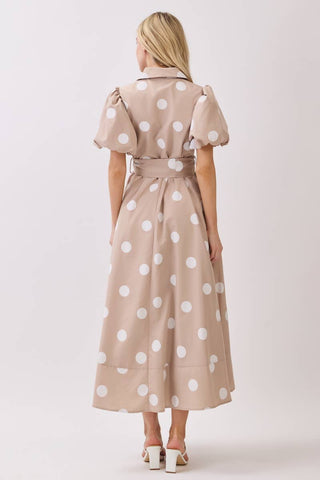 Woman wearing a beige dress with white polka dots on a plain background