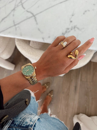 Hand wearing a gold watch and rings on a blurred background