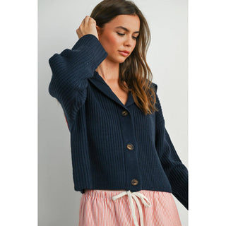 Woman wearing a navy blue cardigan over a striped dress on a plain background