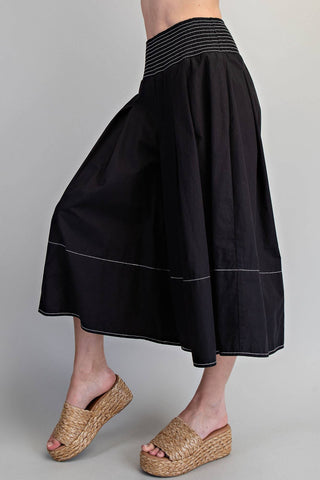 Black skirt with white trim worn by a person on a gray background