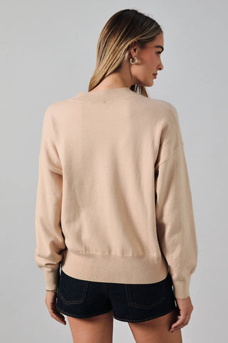A woman shown from the back wearing a light beige crewneck sweater and dark denim shorts against a plain light gray studio background.