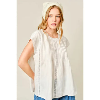 Woman wearing a white lace top and blue jeans against a plain background