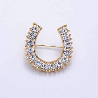Gold horseshoe-shaped brooch with crystal stones on a light gray background