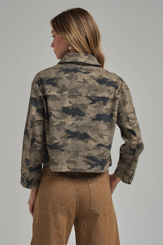 A woman shown from the back wearing a cropped long-sleeve camouflage jacket in shades of brown, beige, and gray, paired with brown pants, against a solid gray studio background.