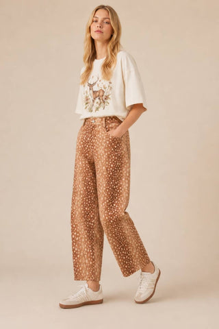 Woman wearing a white t-shirt with a graphic design and brown patterned pants on a beige background