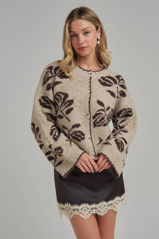 Woman wearing a patterned sweater over a black dress with lace hem on a gray background