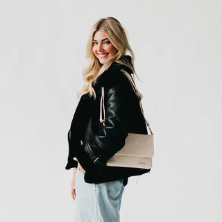 Woman wearing a black leather jacket holding a beige tote bag against a white background