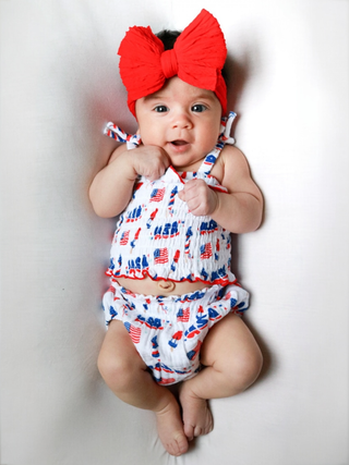 Baby wearing a red, white, and blue outfit with a large bow on a white background