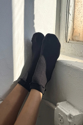 Person wearing black socks sitting by a window with sunlight filtering through.