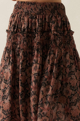 A close-up of a smocked tiered skirt with a dark brown and black floral pattern, showing the texture and design of the fabric.