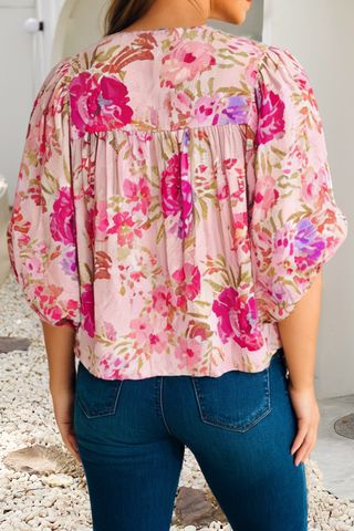 Person wearing a floral blouse with pink and purple flowers on a light background