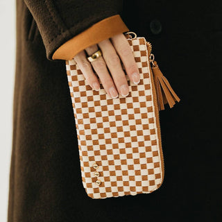 Hand holding a checkered pouch with a tassel against a dark background