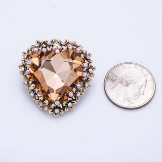 Heart-shaped gemstone brooch with gold accents next to a quarter for scale on a light purple background