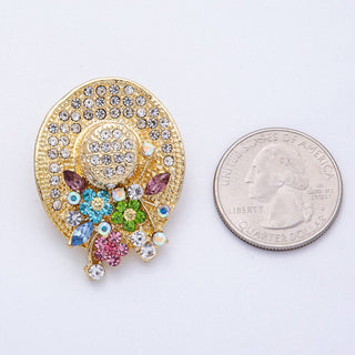 Decorative brooch with colorful gemstones next to a quarter for scale on a white background