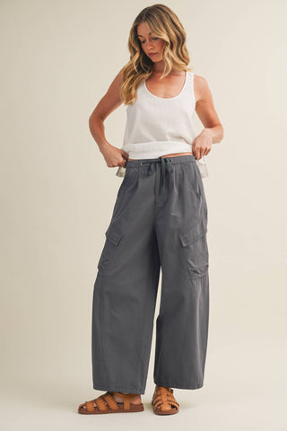 Woman wearing gray cargo pants and a white tank top on a beige background