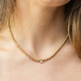 Gold beaded necklace with a heart-shaped pendant on a person's neck