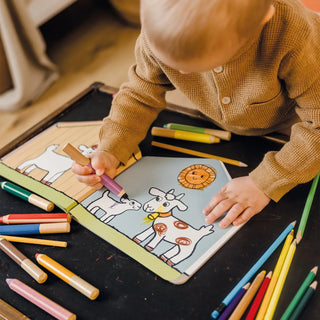 Child coloring a picture of a cow with colored pencils on a table.
