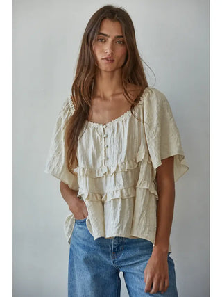 women wearing cream colored ruffled blouse and blue jeans on grey background
