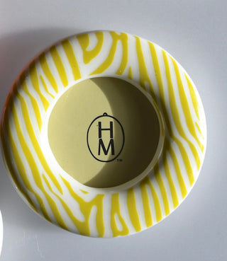 Round ceramic frame with yellow and white pattern and 'H M' logo on a gray background