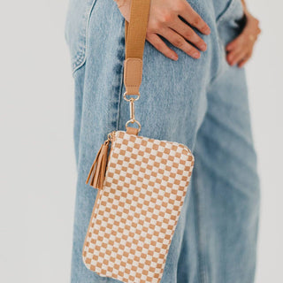 Checkered pouch with a strap held by a person wearing jeans on a light gray background