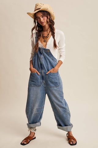 Woman wearing a white shirt, blue denim jumpsuit, and straw hat on a plain background