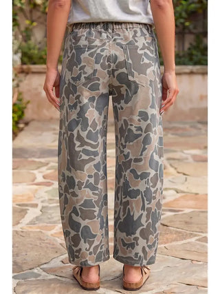A person shown from the back wearing loose wide-leg pants with an abstract camouflage-like pattern in beige, gray, and brown tones, standing on a stone walkway outdoors.