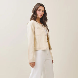 Woman wearing a beige jacket and white pants against a plain background