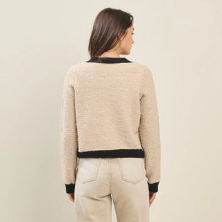 Woman wearing a beige sweater with black trim on a plain background