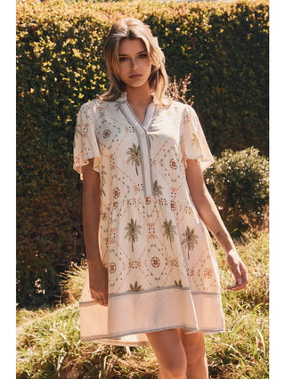 Woman wearing a floral dress standing in a grassy field with bushes in the background