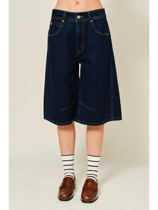 Person wearing dark blue denim shorts on a plain background