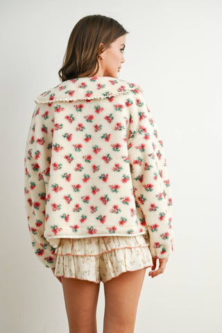 Woman wearing a floral patterned jacket and shorts on a plain background