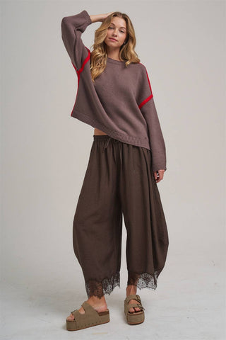 Woman wearing a brown sweater with red accents and wide-leg pants on a plain background