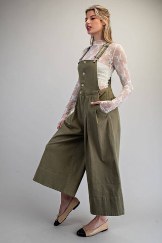 Woman wearing a green jumpsuit with a sheer white top against a plain background