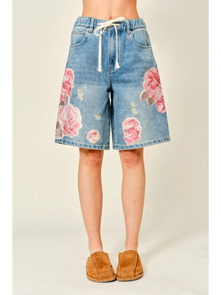 Denim shorts with floral patterns worn by a person on a plain background