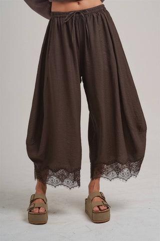 Brown wide-leg pants with lace trim worn by a person on a plain background
