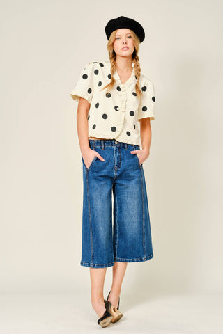 Woman wearing a polka dot blouse, blue jeans, and a black beret on a white background