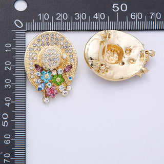 Two decorative brooches with gemstones on a ruler for scale.