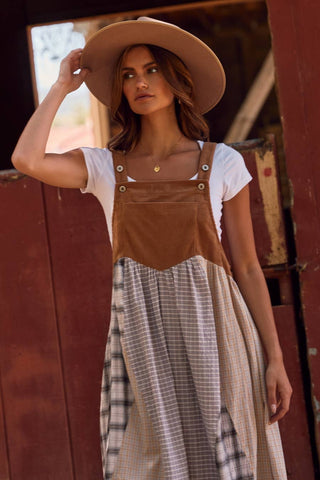 Woman wearing a brown hat, white top, and plaid skirt standing in front of a red wooden wall.