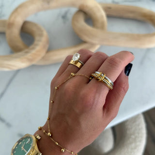 Hand wearing gold jewelry with rings and a watch on a light background